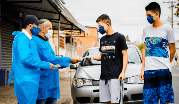 Homens vestidos de jaleco entregam informativo a dois jovens