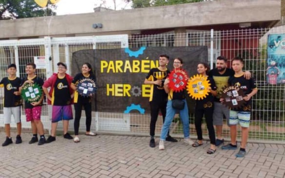Equipe de estudantes em frente a cartaz de parabéns