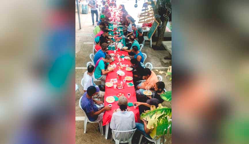 moradores de rua em mesa com toalha vermelha almoçando