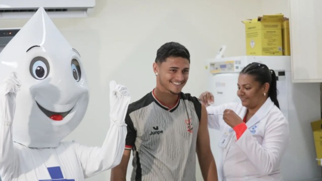 Jogador do Paulista FC tomando vacina ao lado de Zé Gotinha.