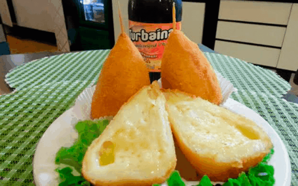 Coxinha de queijo cortada ao meio, com garrafa de Turbaína atrás.