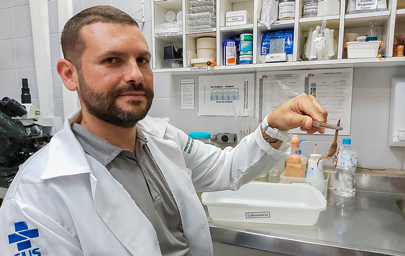 Foto do veterinário segurando escorpião em laboratório, por meio de uma pinça