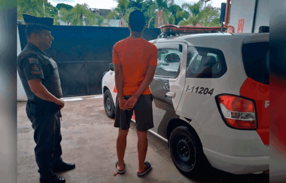 Homem de costas, algemado, com viatura da Polícia ao fundo