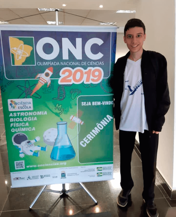 Mateus ao lado do banner da Olimpíada Nacional de Ciências