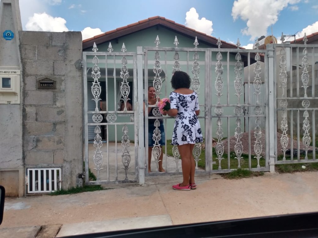 Thauany entrega flor a uma moradora pelo portão de casa