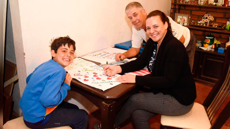 Victor ao lado do pai e da mãe fazendo trabalhos da escola
