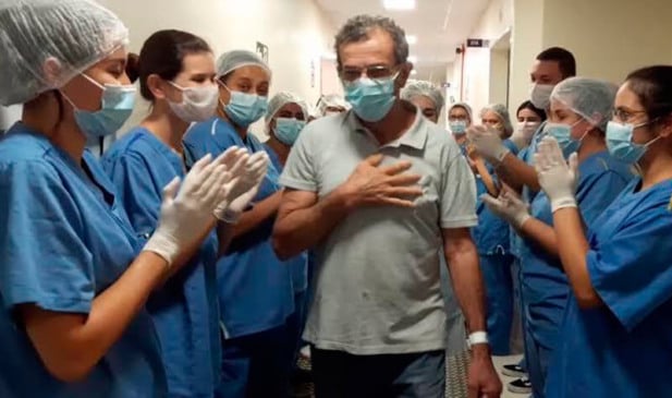 Homem sai do Hospital passando por corredor de profissionais de saúde que batem palmas em comemoração à recuperação
