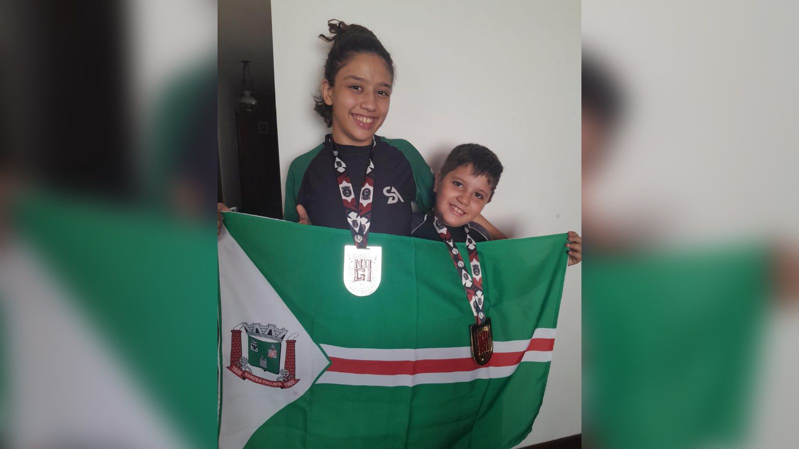 Irmãos de Várzea Paulista com medalhas e bandeira da cidade.