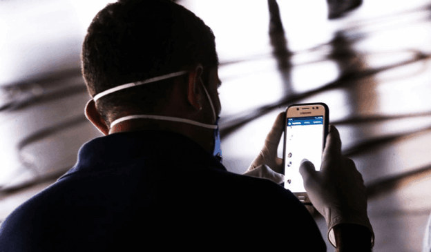 Pessoa com máscara mexe no celular