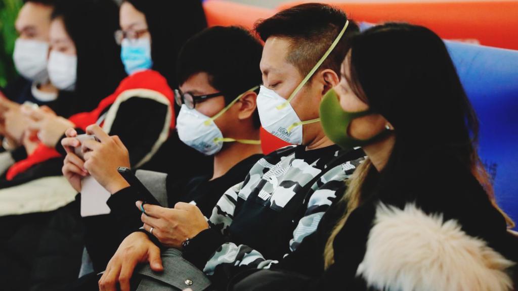 Jovens orientais usam máscaras enquanto esperam sentados em fila