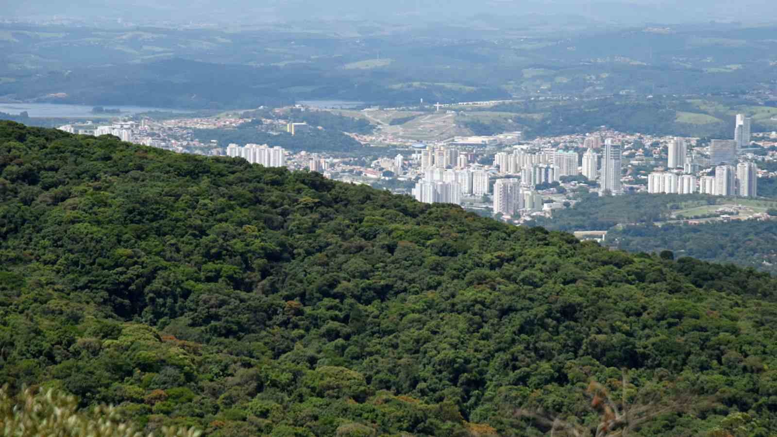 Vista aérea de Jundiaí com a Serra do Japi em primeiro plano e prédios da cidade ao fundo.