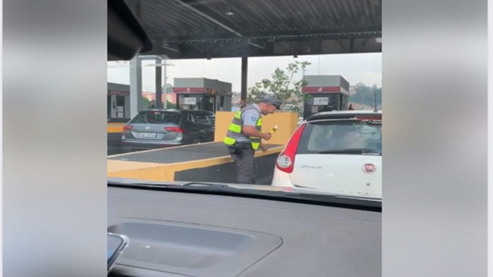 policial encostado no carro realizando bafometro