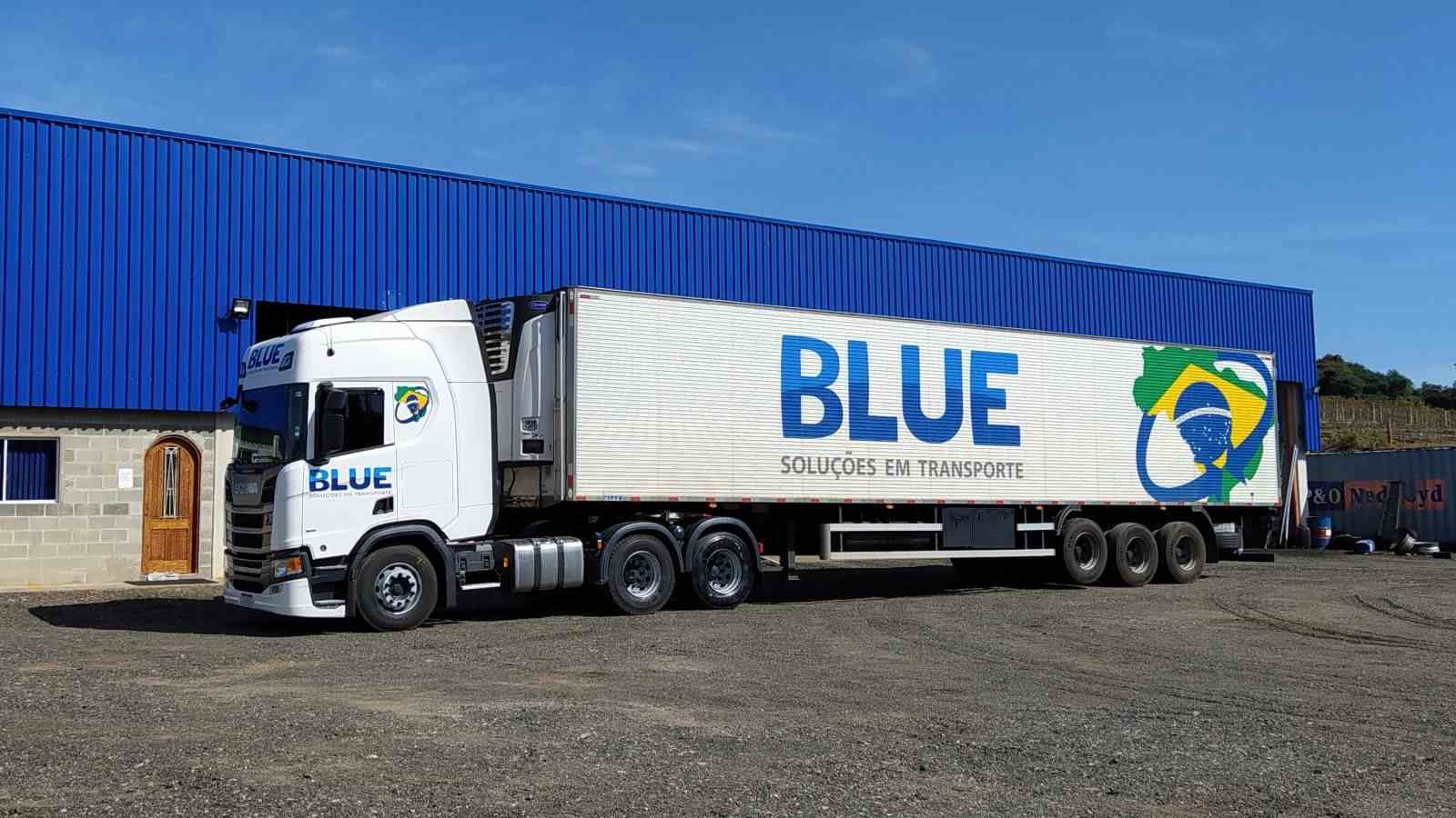 Caminhão da Blue Transportes estacionado em frente à sede da empresa em Itupeva, com logotipo e mapa do Brasil estampados na lateral do baú.