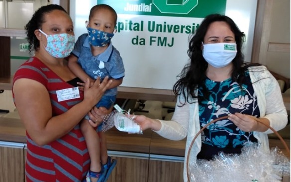 Mulher entrega kit coronavírus a outra, com filho no colo