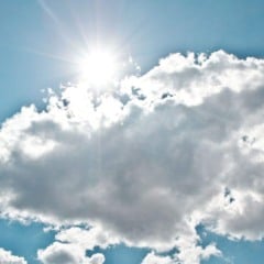 Sol forte atrás de nuvens brancas em céu azul, representando variação entre sol e nuvens.