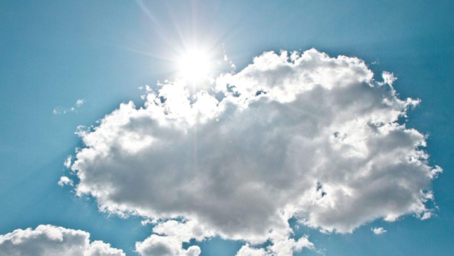 Sol forte atrás de nuvens brancas em céu azul, representando variação entre sol e nuvens.