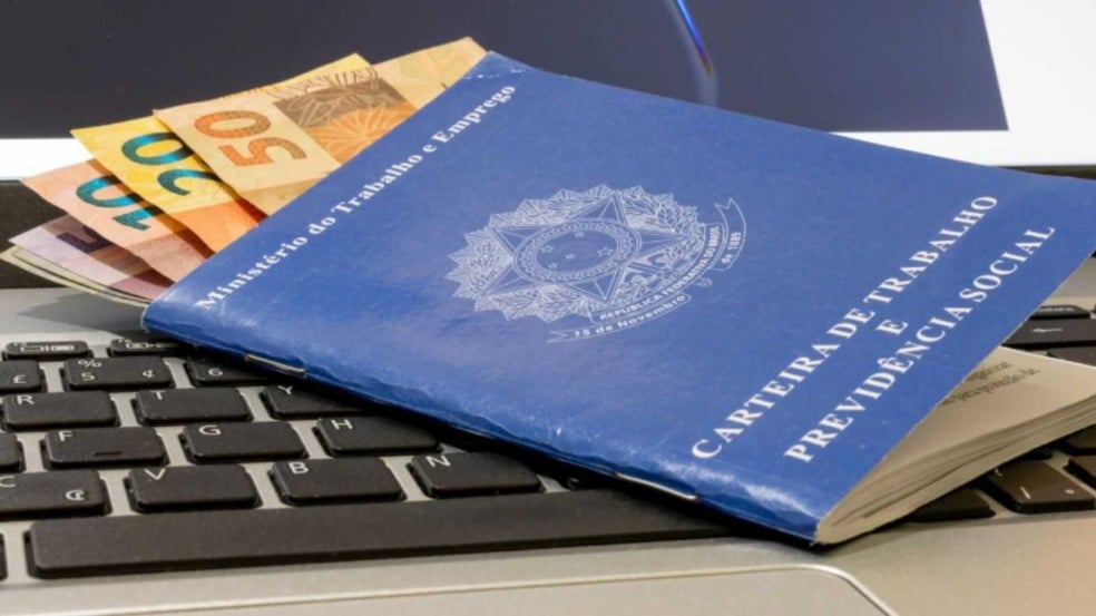 Carteira de trabalho com dinheiro e notebook.