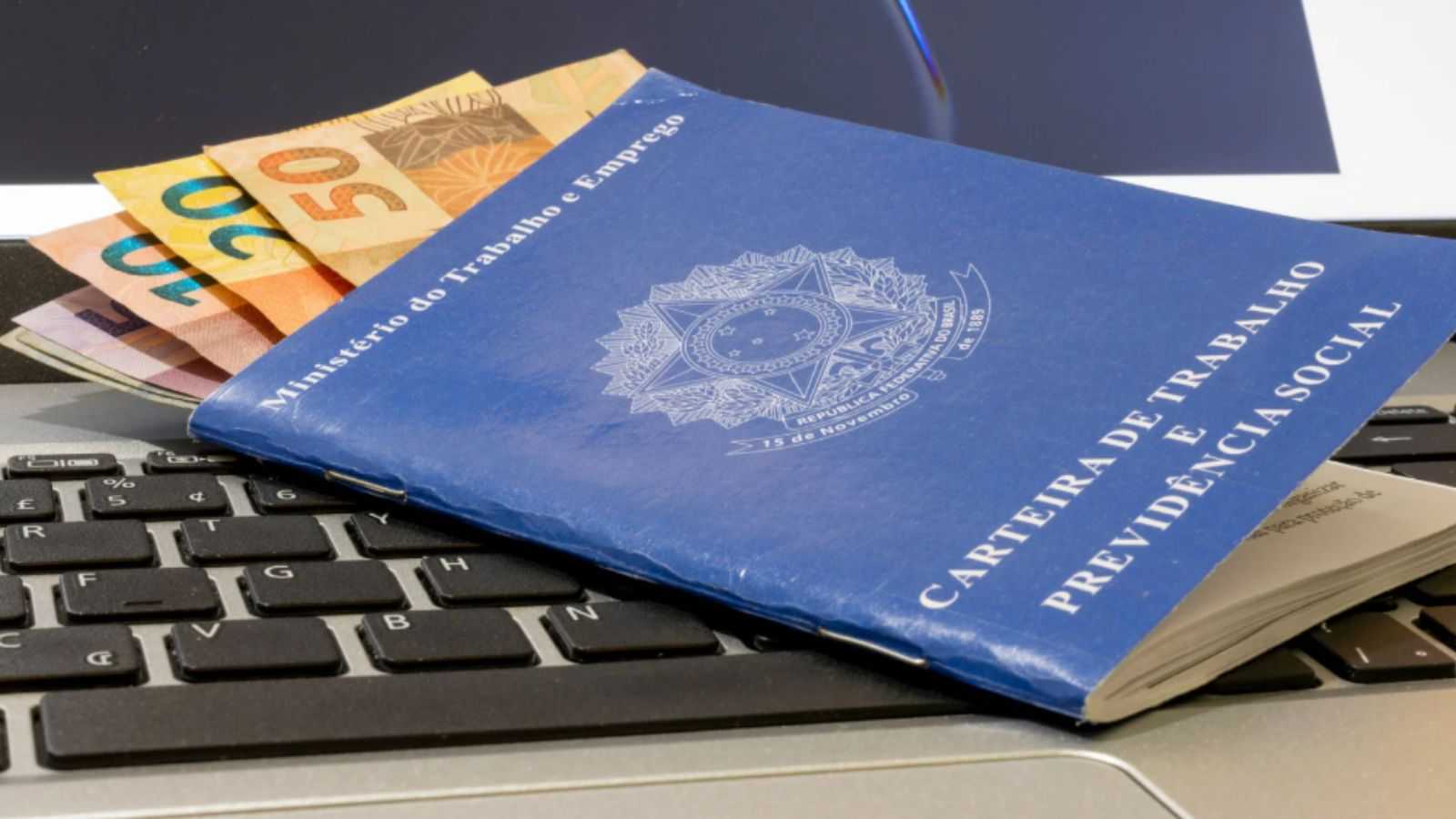 Carteira de trabalho com dinheiro e notebook.