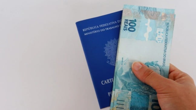 Carteira de trabalho com cédulas de 100 reais.