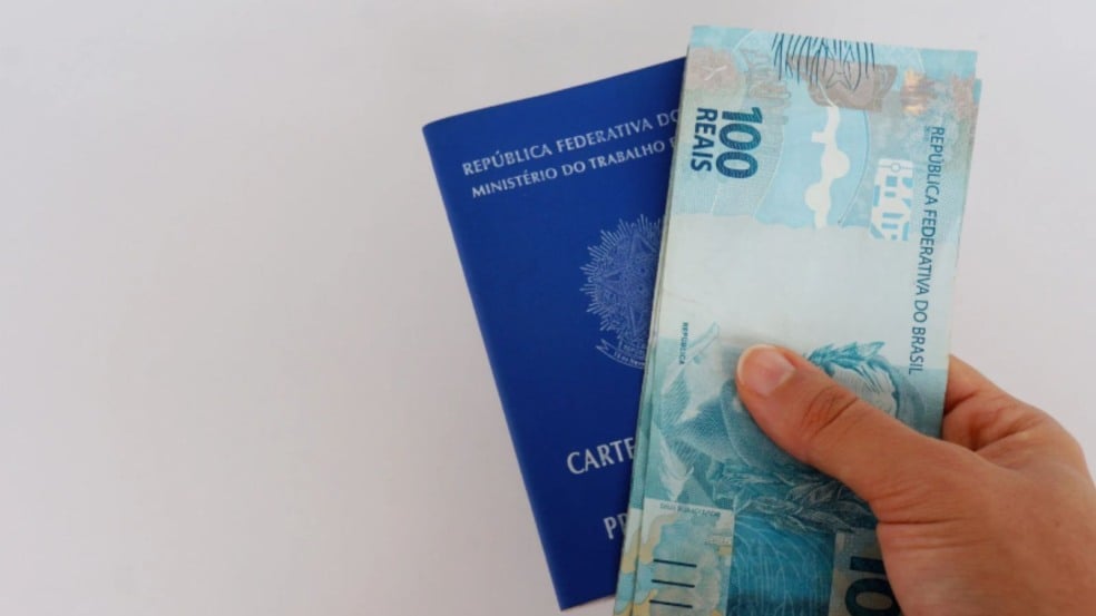 Carteira de trabalho com cédulas de 100 reais.