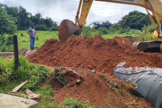 Chuvas em Itupeva: escavadeira realiza reparos em estrada de terra danificada, com operário observando o trabalho no local.