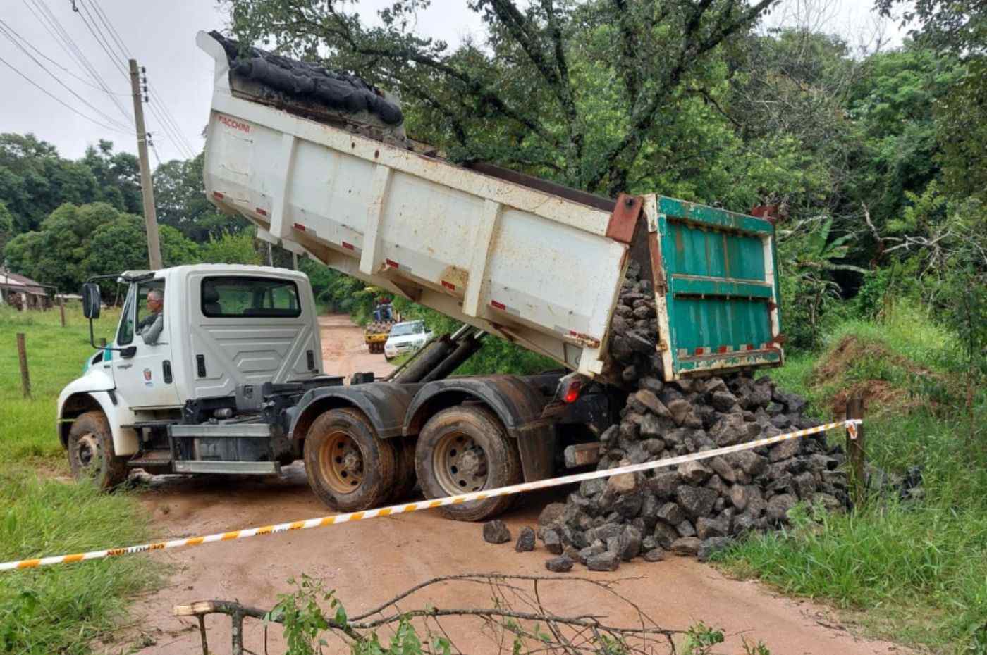 Chuvas em Itupeva: caminhão basculante despeja pedras em estrada de terra danificada para recuperação e manutenção da via.