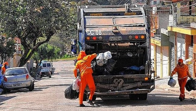 Caminhão de lixo com coletores com sacos de lixo na mão para colocar no caminhão