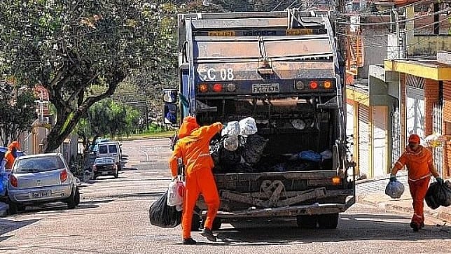 Caminhão de lixo com coletores com sacos de lixo na mão para colocar no caminhão