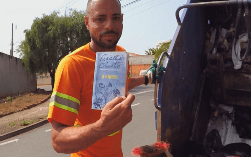 Luciano vestido de coletor segura livro na mão
