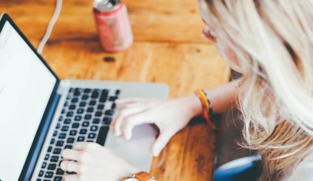 Foto de mulher loira mexendo em notebook, à esquerda tem uma lata vermelha de bebida.