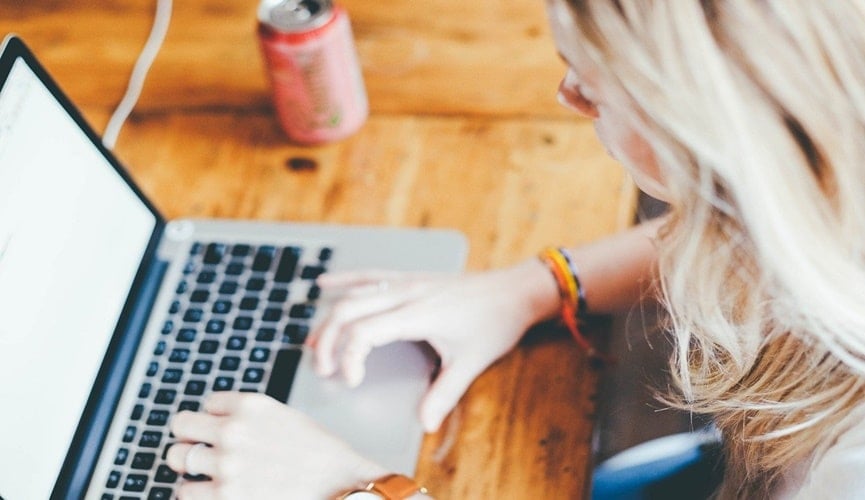 Foto de mulher loira mexendo em notebook, à esquerda tem uma lata vermelha de bebida.