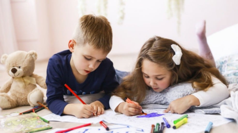 Crianças deitadas no chão, desenhando