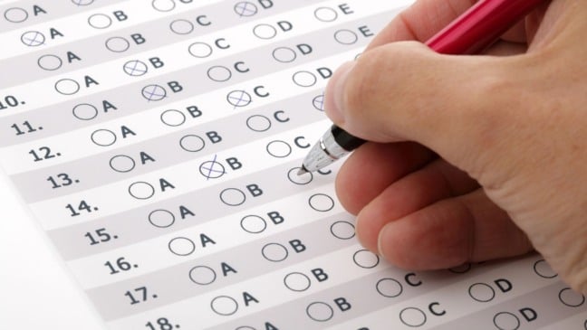 Mão preenchendo cartão-resposta de exame de múltipla escolha com caneta.