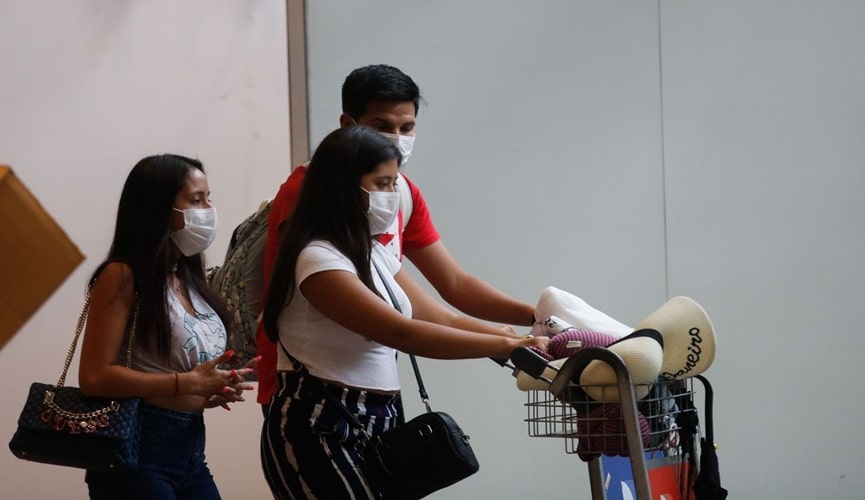 Duas mulheres morenas de cabelos longos pretos, com homem moreno de cabelo curto, saindo de aeroporto com máscaras Duas mulheres morenas de cabelos longos pretos, com homem moreno de cabelo curto, saindo de aeroporto com máscaras