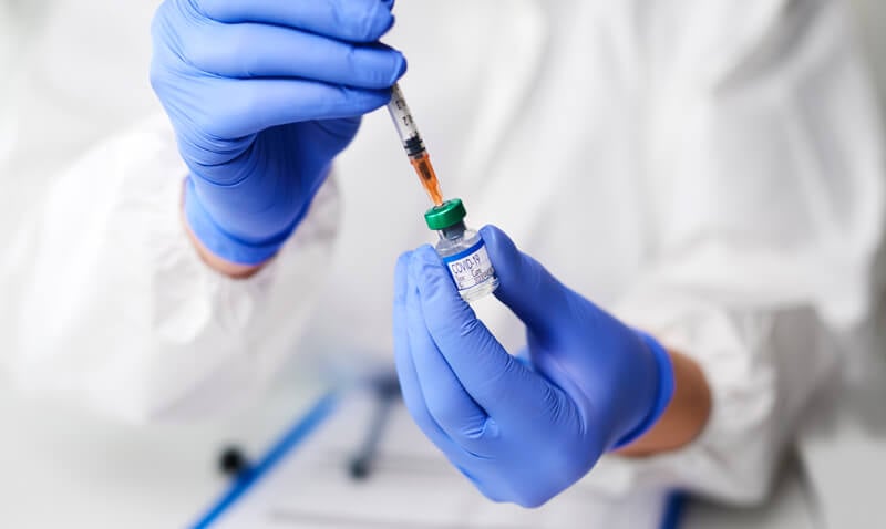 Seringa pega substância vacinal de potinho de vidro