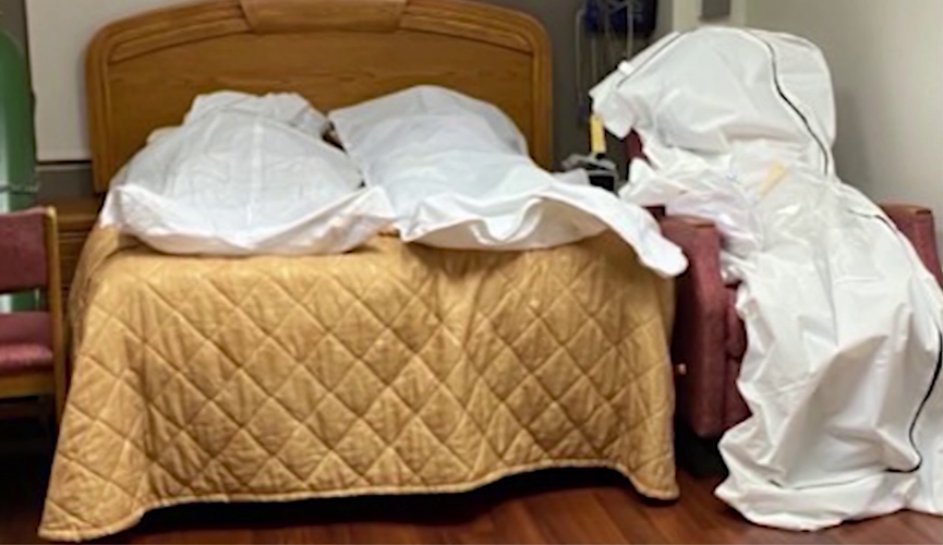 Na foto, dois corpos foram colocados em uma cama, lado a lado, e outro em uma poltrona no mesmo quarto. Todos os três corpos estão em sacos brancos.