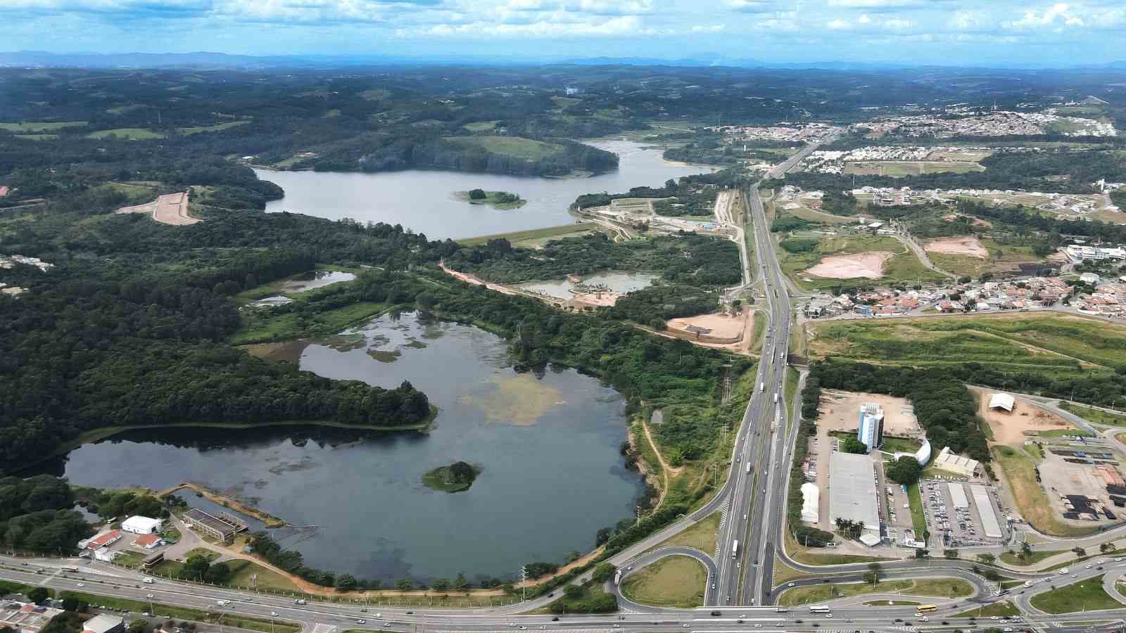 Vista aérea da represa de Jundiaí ao lado da Rodovia Anhanguera, cercada por áreas verdes e bairros urbanos.