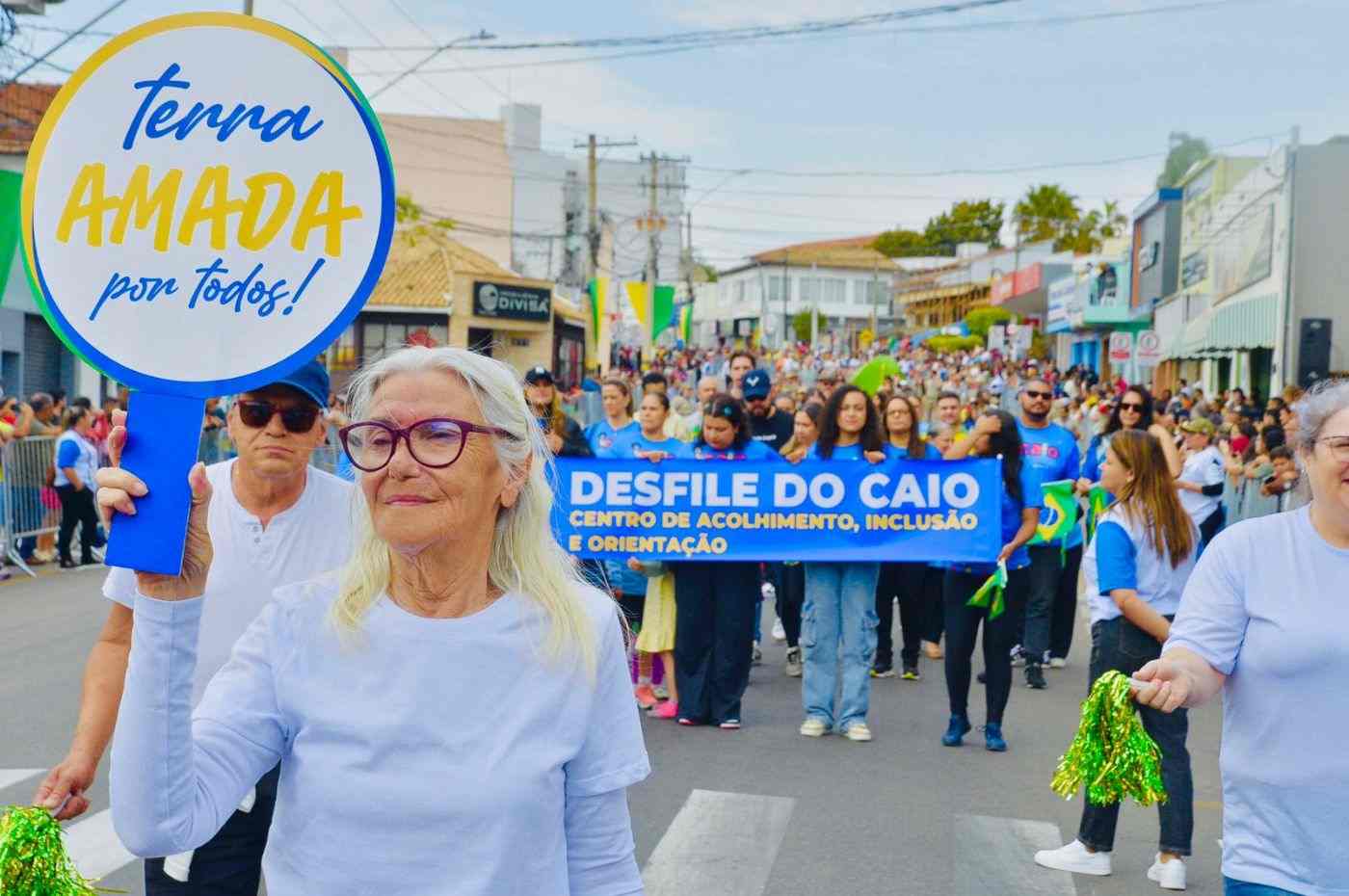 Idosa participa do desfile do CAIO em Itupeva segurando placa com a frase “Terra amada por todos”