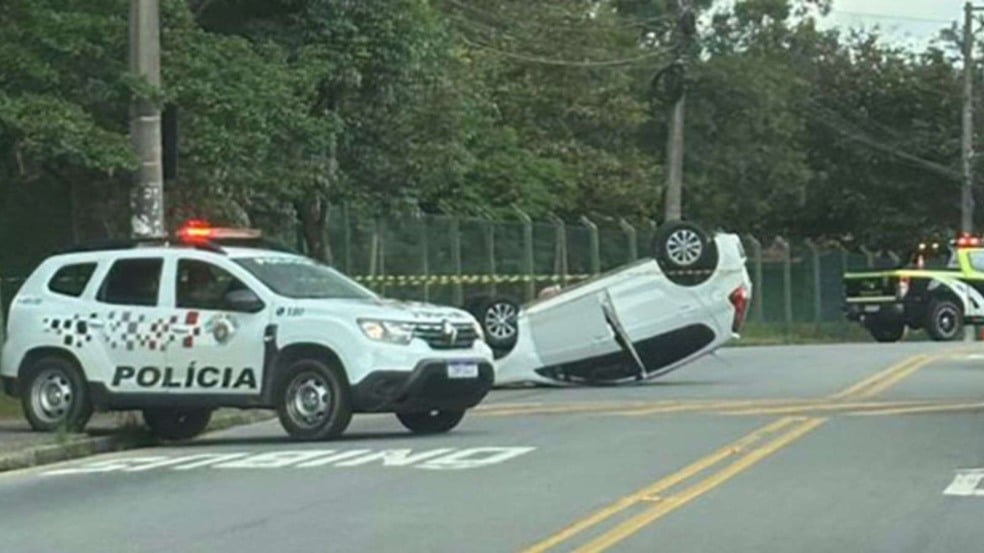 Carro capotado ao lado de viatura da Polícia Militar.