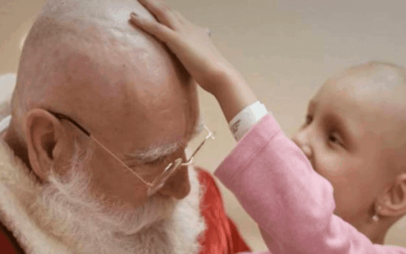 Menina careca passando a mão na cabeça do Papai Noel, já sem cabelo