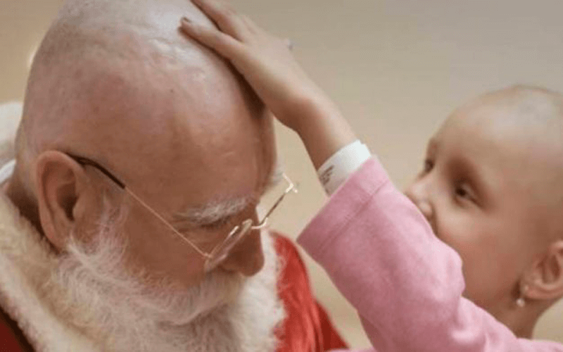 Menina careca passando a mão na cabeça do Papai Noel, já sem cabelo