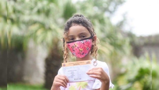 Criança segurando seu comprovante de vacina contra Covid19