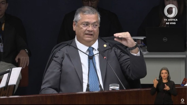 Ministro Flávio Dino, do STF, fala durante sessão e gesticula com a mão levantada, enquanto uma intérprete de Libras aparece no canto inferior direito.