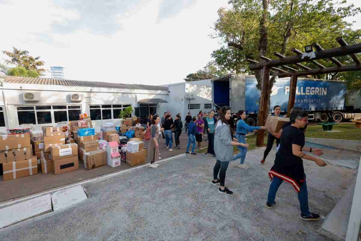 Doações de Jundiaí para crianças vítimas das enchentes no RS. Voluntários carregam caixas de mantimentos e brinquedos para um caminhão de transporte.