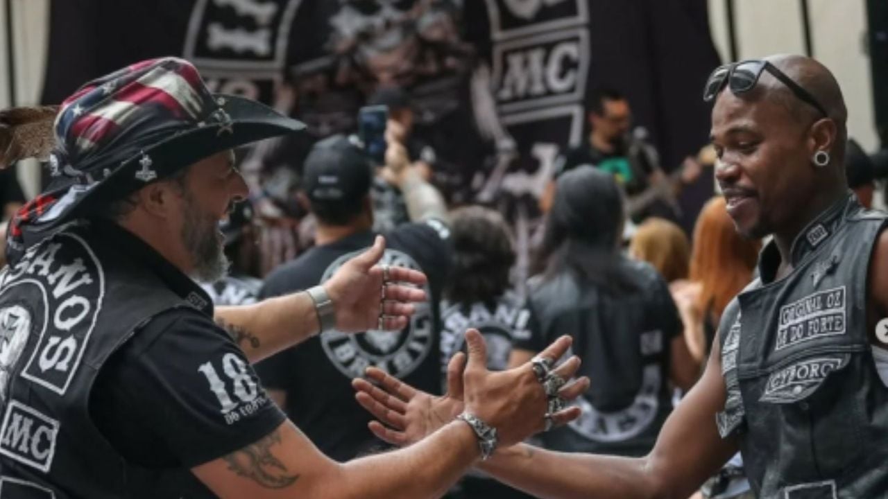 Dois homens em evento de motociclistas cumprimentando-se. Um usa chapéu com estampa da bandeira americana.