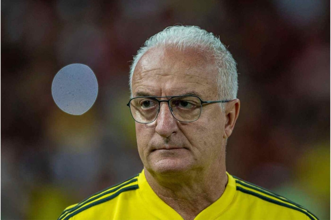 Técnico de futebol Dorival Júnior com expressão séria, usando camisa amarela e óculos, durante partida oficial.