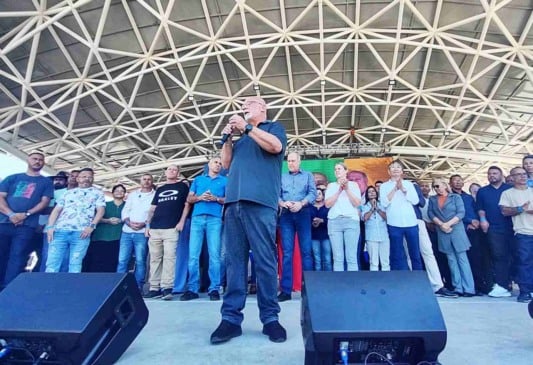 Dr. Luiz Braz discursando em convenção política, rodeado por apoiadores no palco coberto, promovendo sua reeleição em Campo Limpo Paulista.