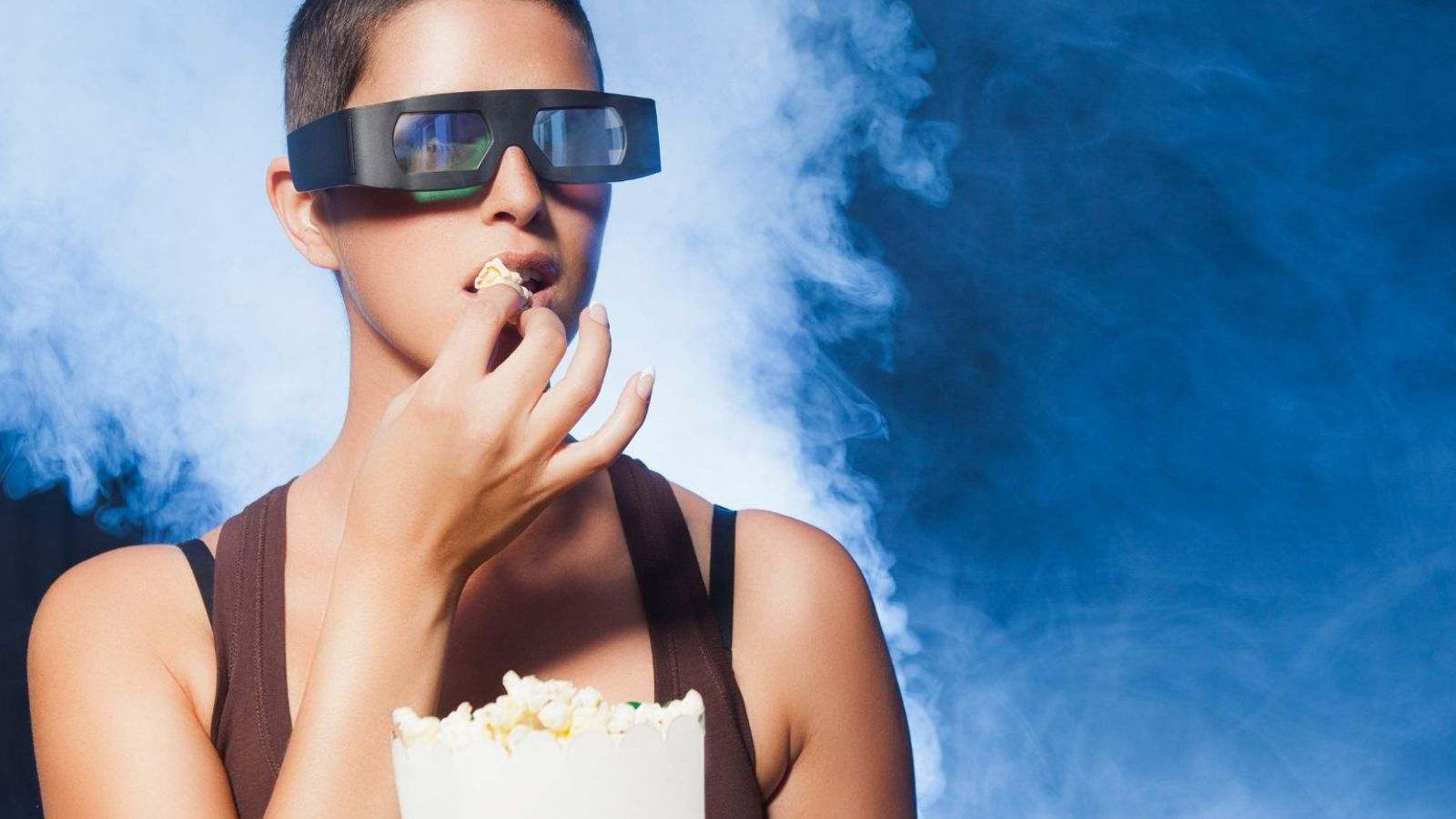 Mulher comendo pipoca com óculos 3D.