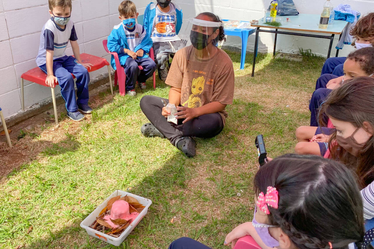 professora rodeada por seus alunos em uma aula inovadora fora da sala