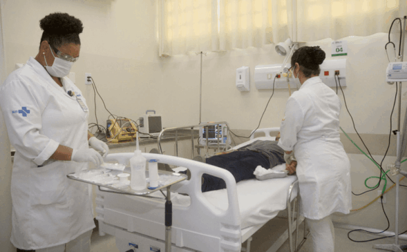 Enfermeiras realizando exame em paciente que está deitado em cama hospitalar